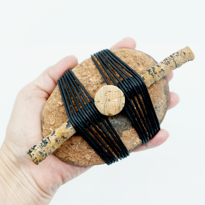 Entwined wrapped rock with stick and cork button in a women's hand