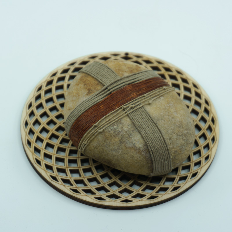 A wrapped rock called Grounding on a wood cut patterned plate
